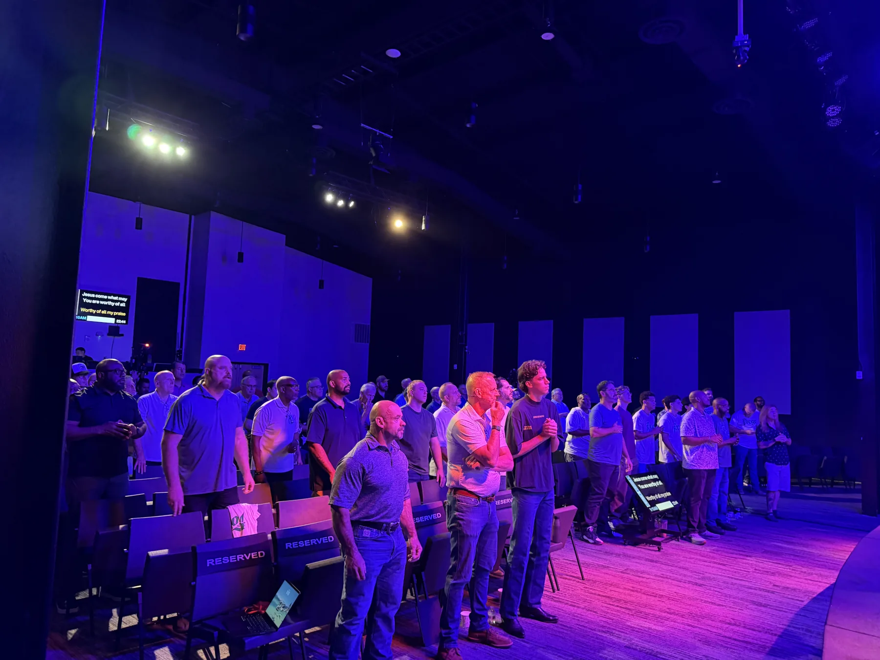 Men raise their hands in worship across the Oaks Church auditorium