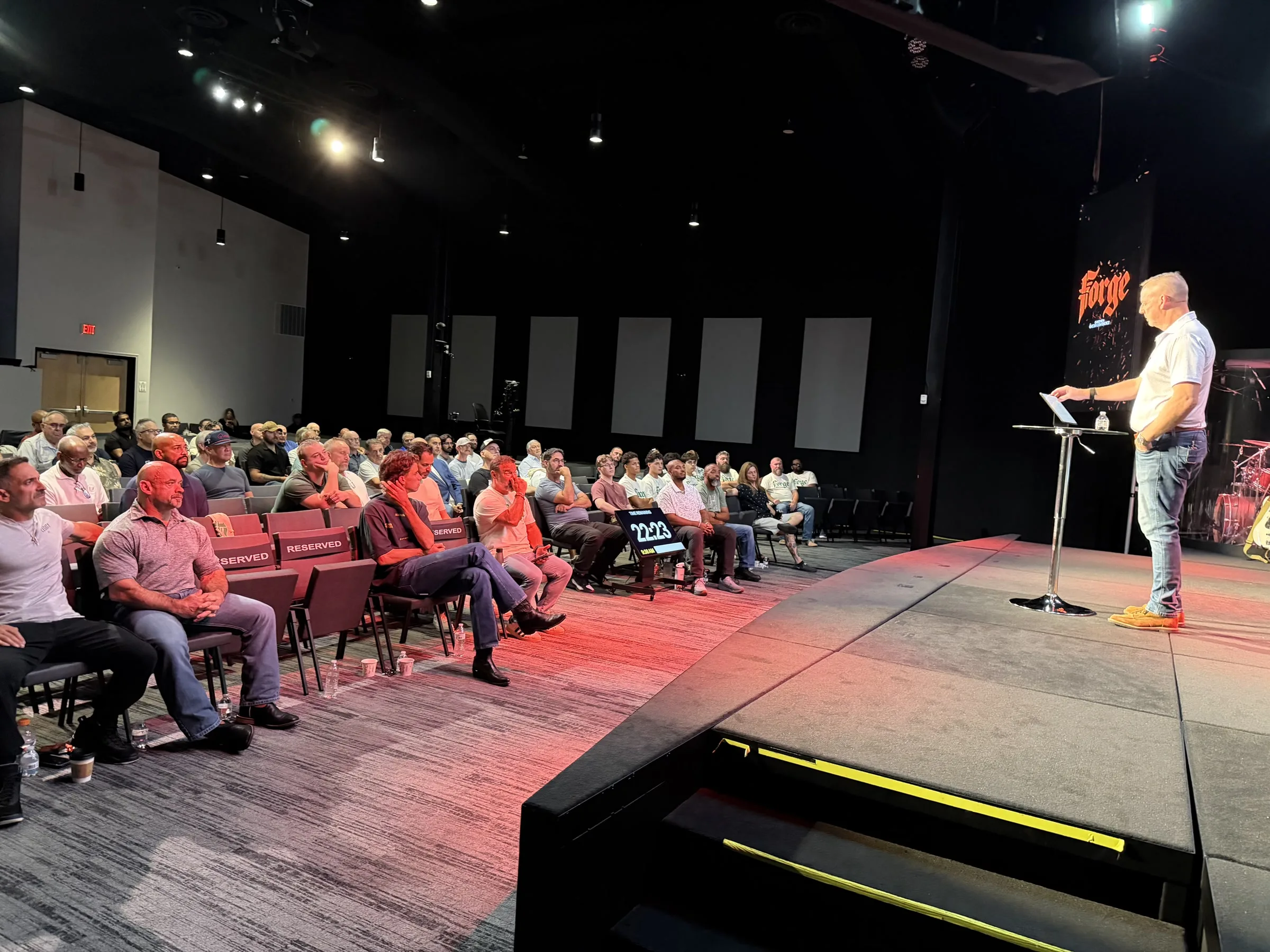A speaker addresses men seated near the Forge One Day stage