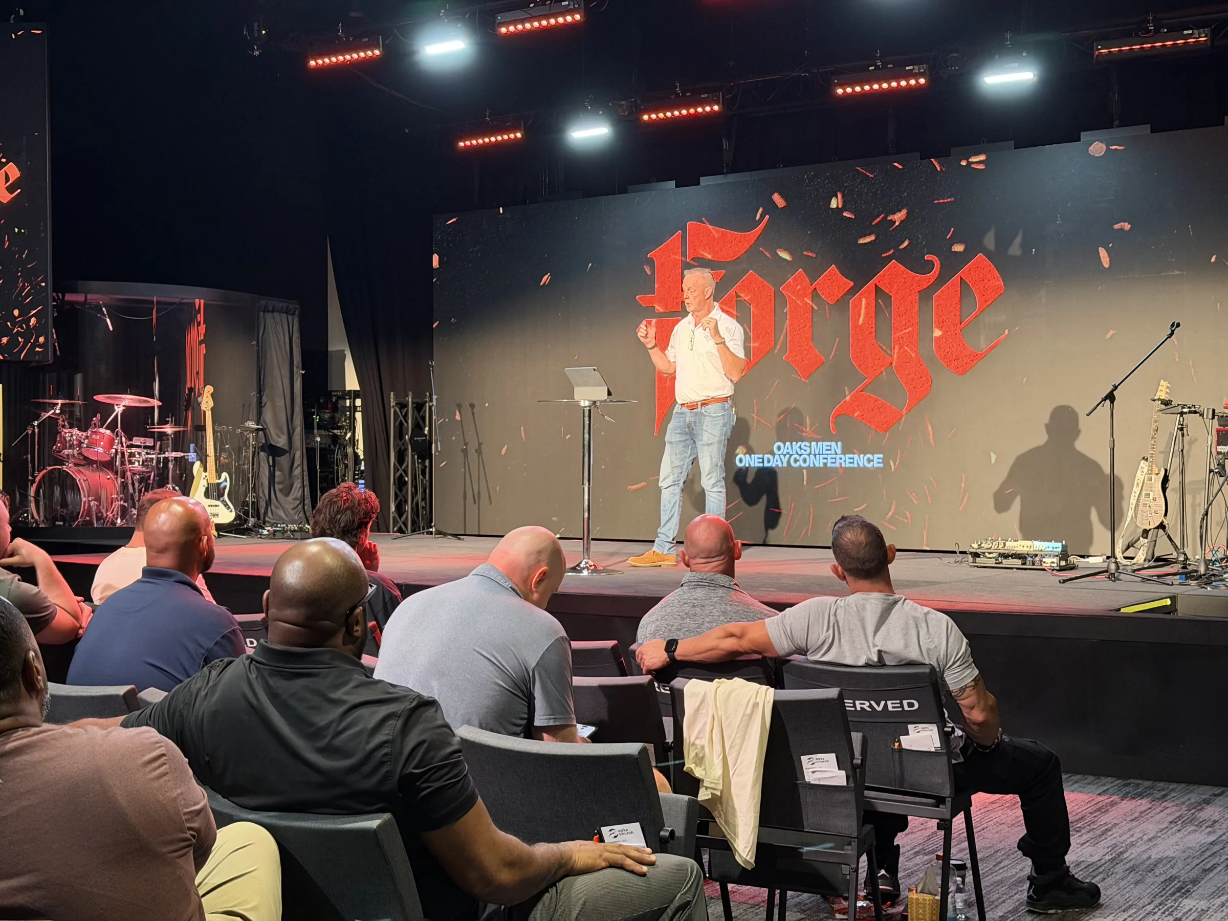 Men listen as a speaker teaches beneath the Forge backdrop