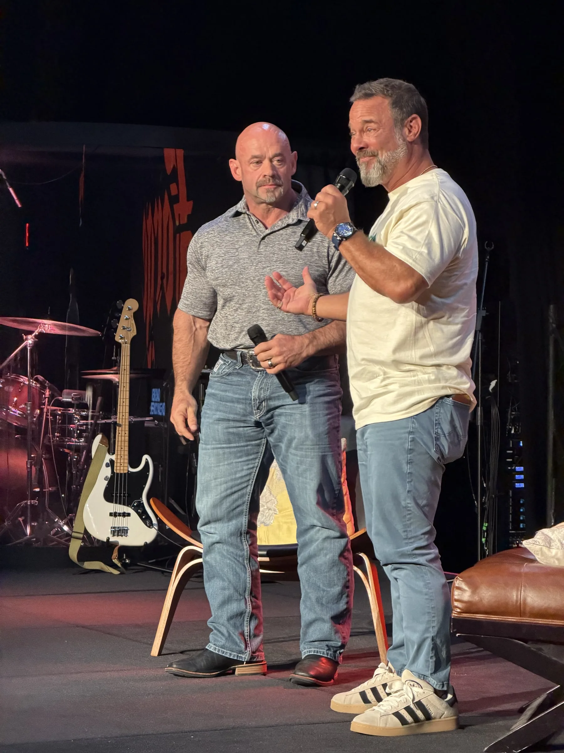 Two men stand together as one speaks on the Forge One Day stage