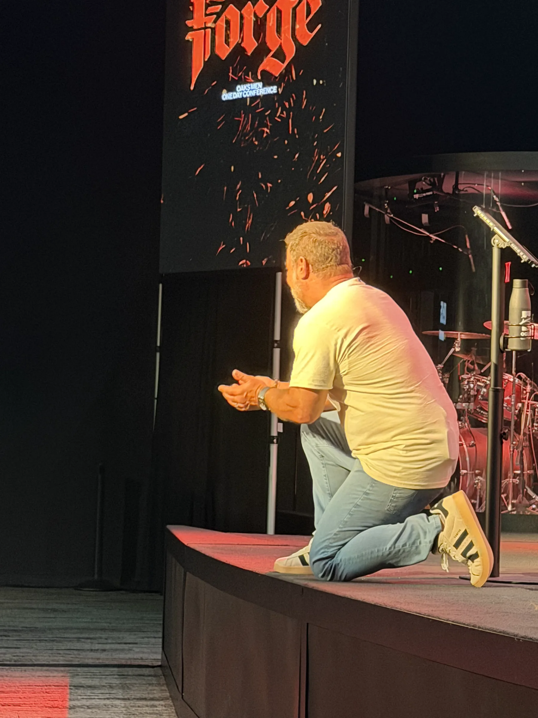 A man kneels at the edge of the Forge One Day stage beneath the Forge logo
