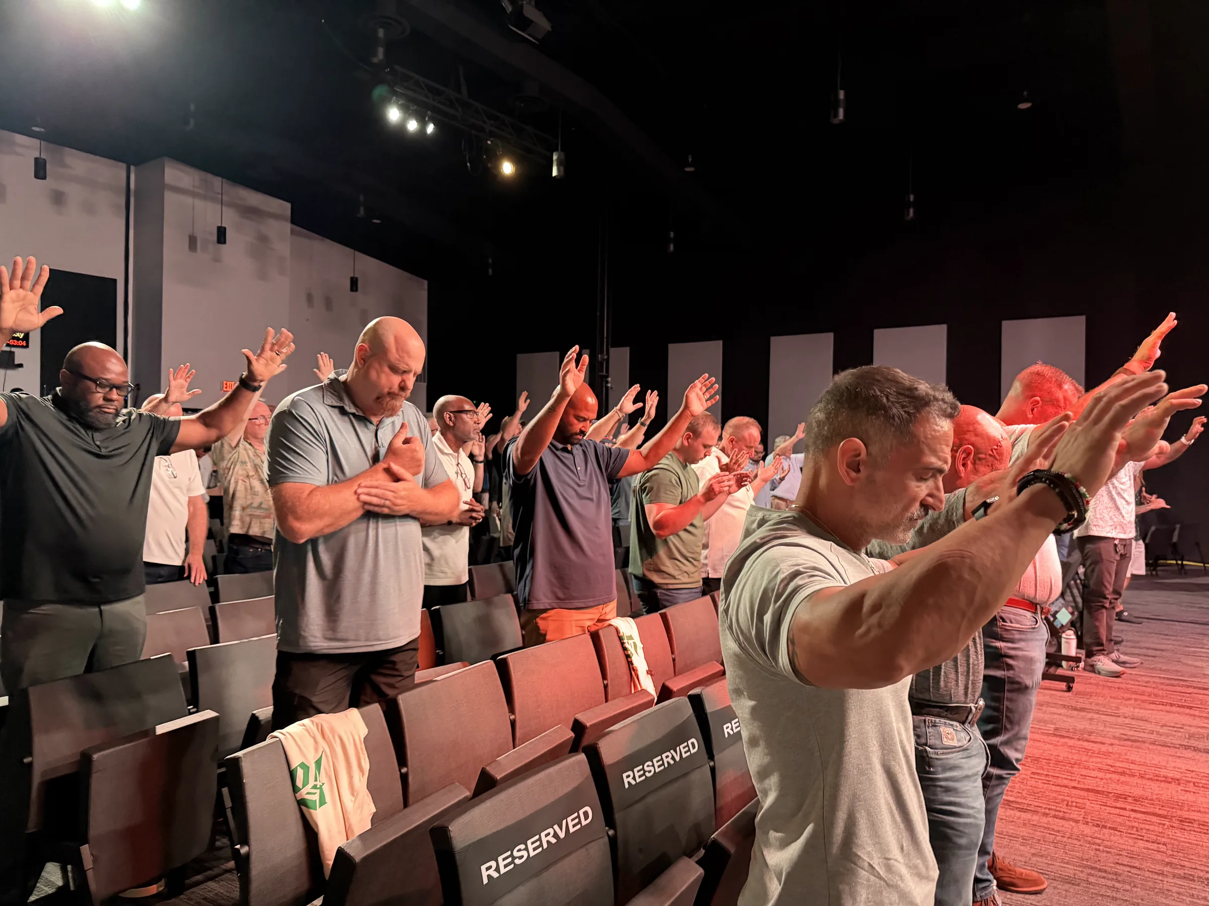 Men stand with bowed heads and raised hands during prayer at Forge One Day