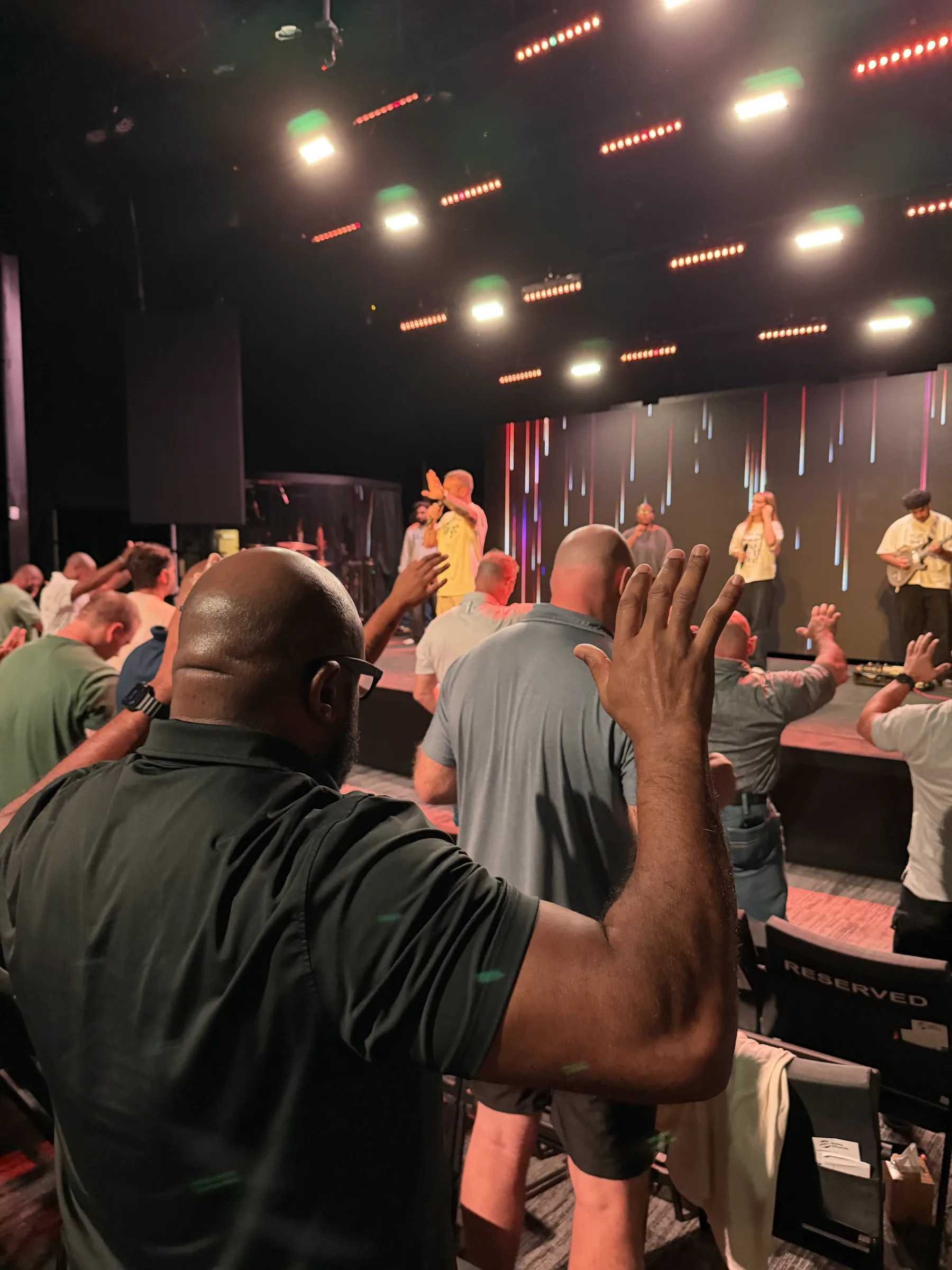 A man raises his hand while the worship team leads from the Forge One Day stage