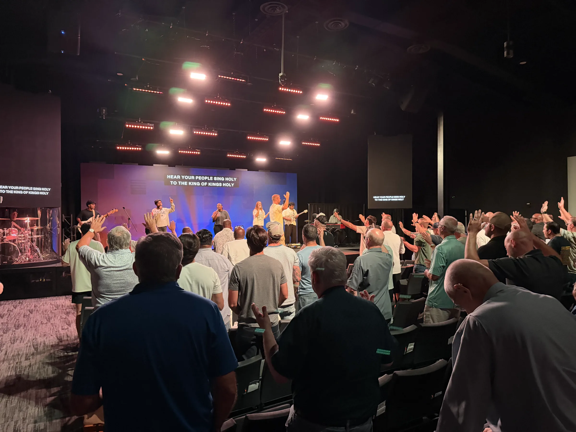The worship team leads from the stage as men across the room lift their hands