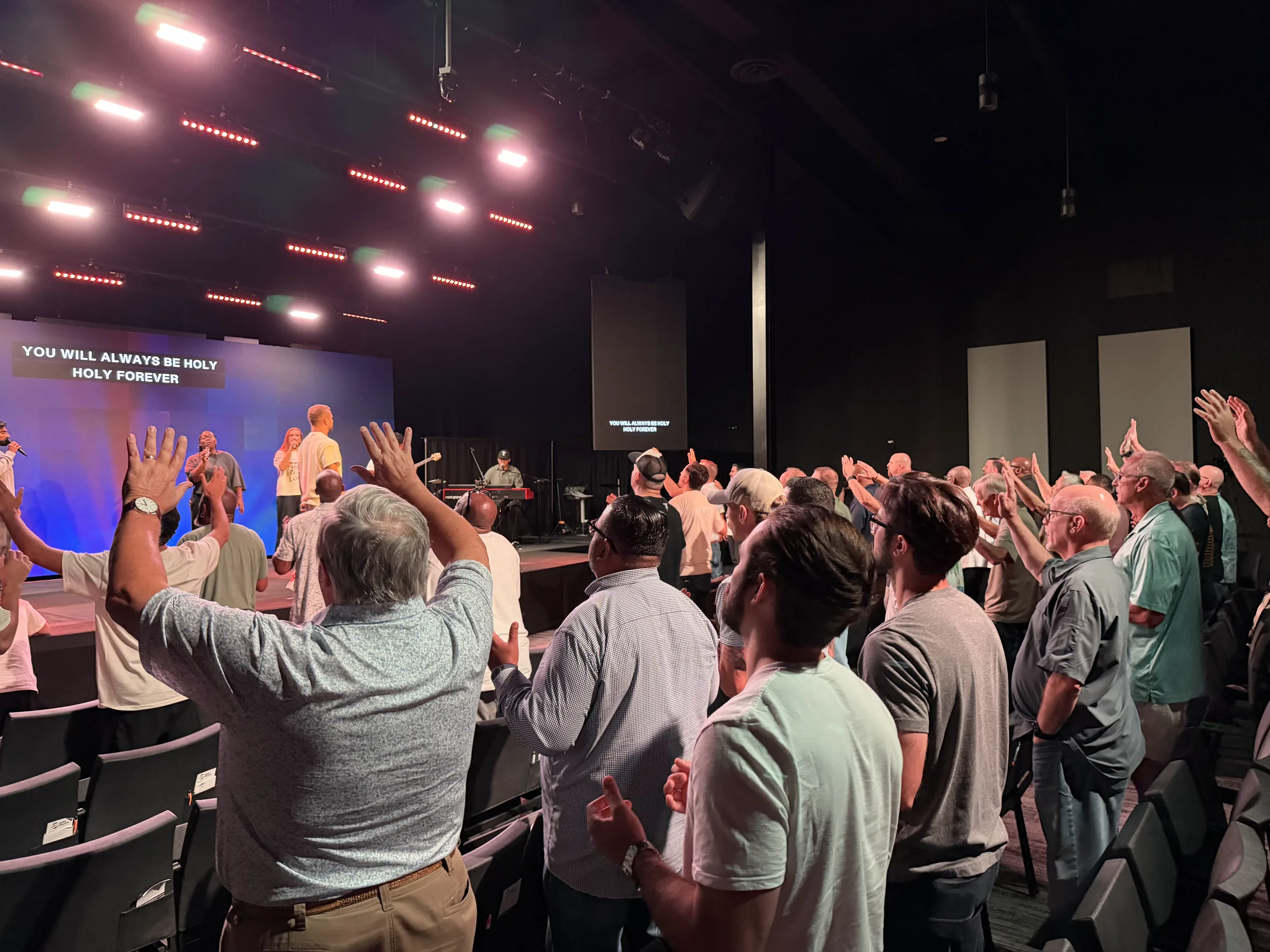 Men gather near the Forge One Day stage with hands raised during closing worship